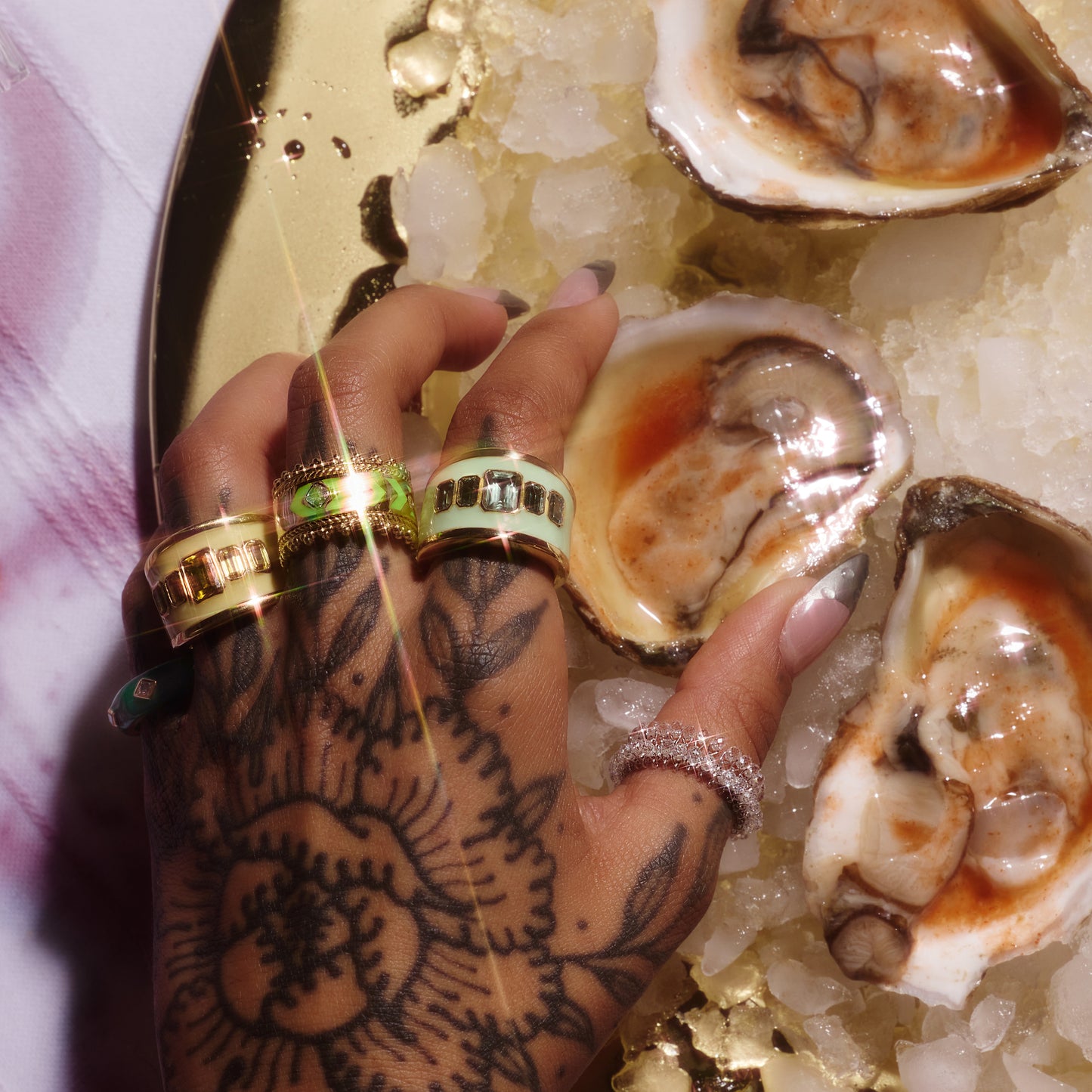 18ct yellow gold ring with green enamel and emerald cut lab-grown sapphires, worn on a hand holding oysters.