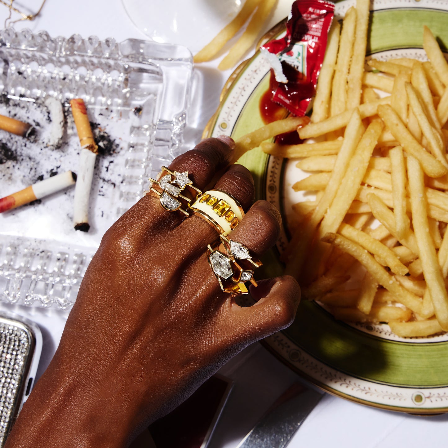18ct yellow gold ring with yellow enamel and emerald cut lab-grown yellow sapphires, worn on a hand grabbing fries.