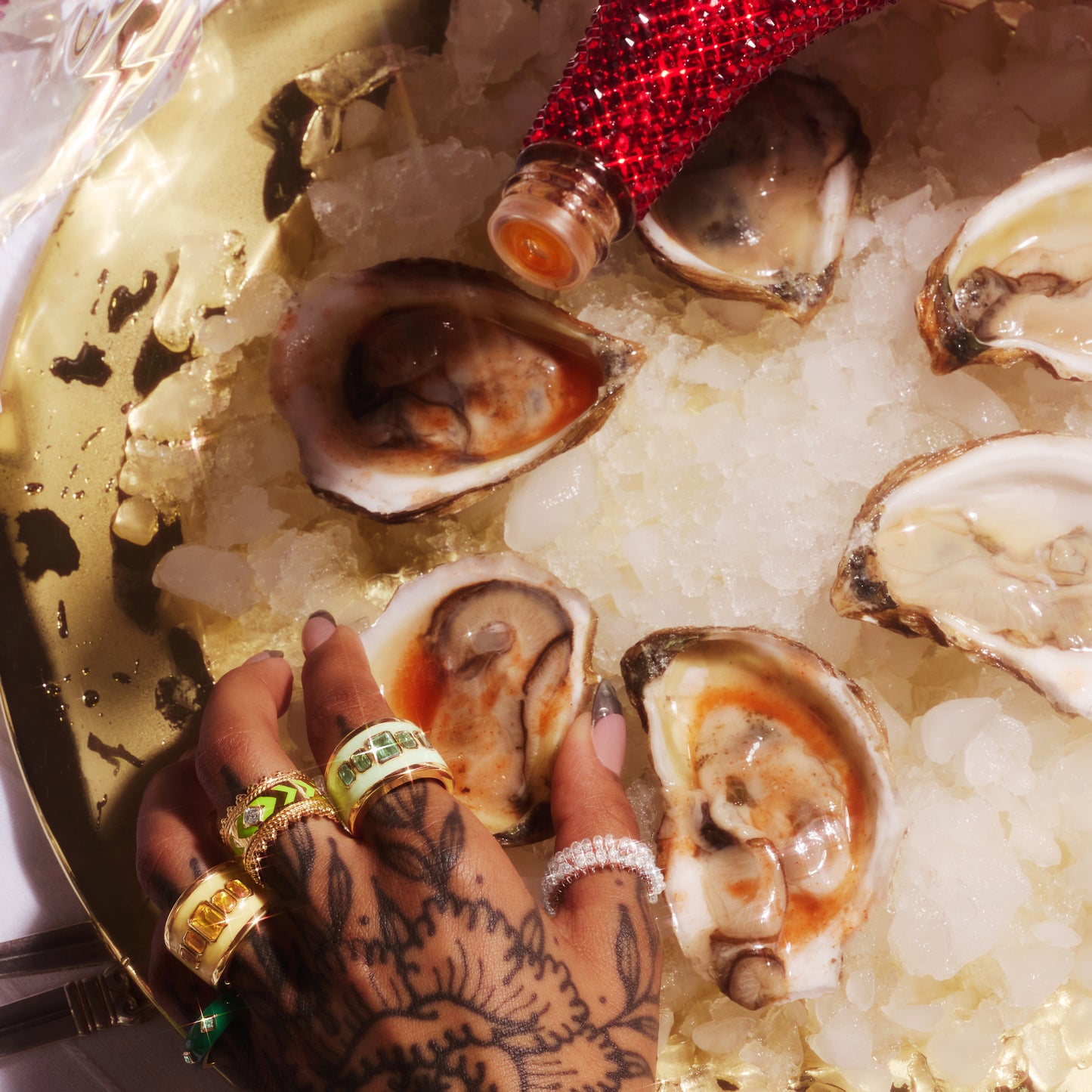 Hand reaching for oysters wearing the VENEZIA ring in 18ct yellow gold with neon green enamel and lab-grown diamonds.